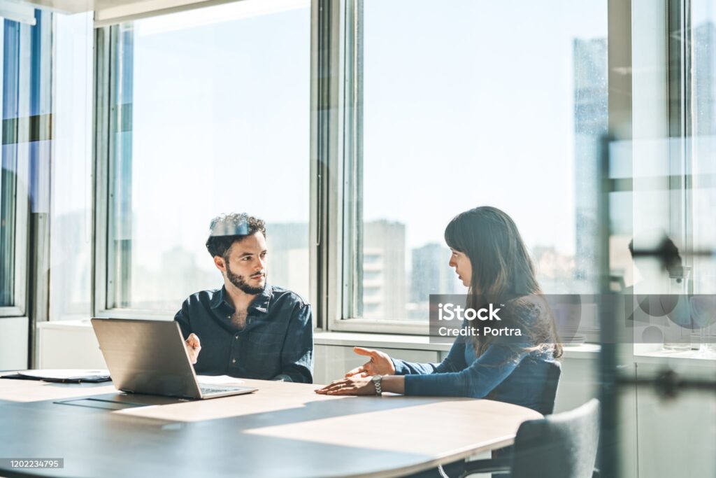 Businesswoman explaining businessman during meeting. Male and female colleagues are discussing at conference table. They are sitting in board room.